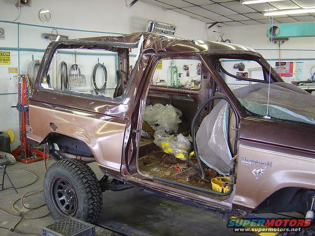 Brown Ford Bronco II body with doors removed, interior gutted, and roof damaged