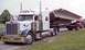 1979 Ford Bronco - A white Peterbilt semi-truck transports a massive concrete beam, with another red truck visible behind it.