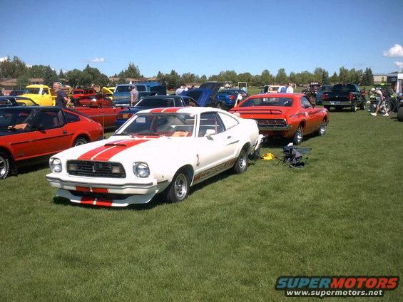 1978 Ford Mustang II with red stripes parked on grass at a car show
