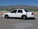 1999 Ford Crown Victoria - Side view of a white sedan parked outdoors with a mountainous landscape behind it.