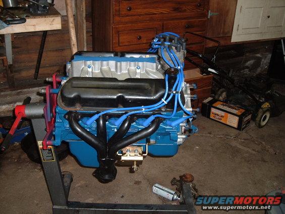 Blue engine on stand with black exhaust manifolds and blue spark plug wires