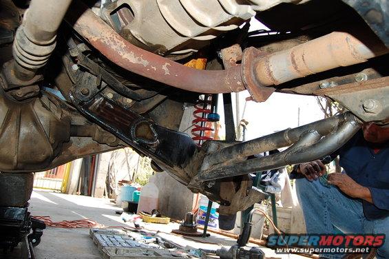 Undercarriage view of a vehicle's suspension and exhaust system, with a person working on it