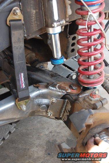 Close-up of a vehicle's suspension with a red coilover shock, a black strap with 'MasterCraft' text, and other metal components