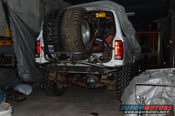 Rear view of a white SUV with two large spare tires mounted on a custom rack, covered in a tarp