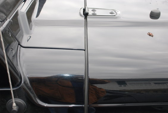 close-up of black vehicle's door and hood seam with reflections of landscape