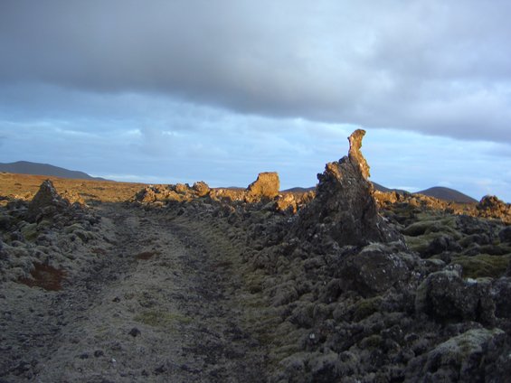 Rocky, moss-covered landscape with a dramatic rock formation under a cloudy sky