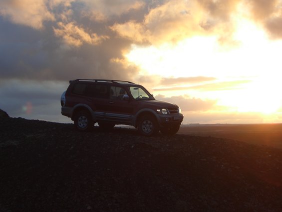 Red SUV parked on a rocky incline during sunset