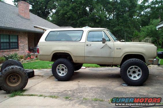 Lifted 1978 Dodge Ramcharger SUV parked on driveway, side view. Spare tires are stacked nearby