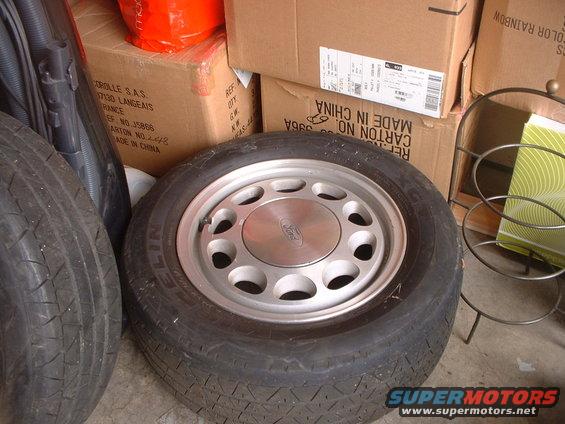 Close-up of a Ford-branded wheel with a tire, resting on the floor next to other tires and boxes