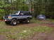 1991 Ford Bronco - A lifted Ford Bronco sits parked in a wooded area beside a campsite.