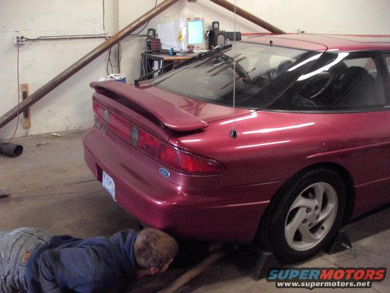 guy working under a red coupe, possibly a 1990s model