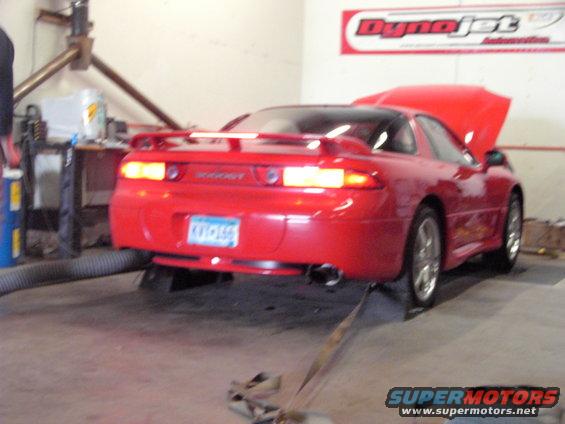 Red sports car with hood up on a dynamometer, showing a spoiler and license plate
