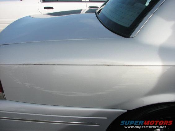 Silver 2003 Ford Crown Victoria rear quarter panel and trunk lid, showing a chrome trim line and minor scuffs