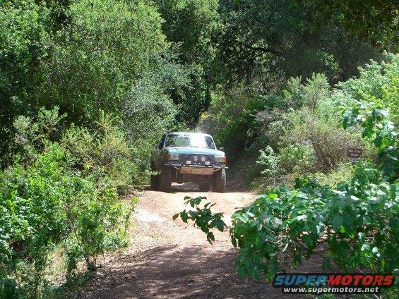 Green off-road truck on a dirt path, modified bumper and lights
