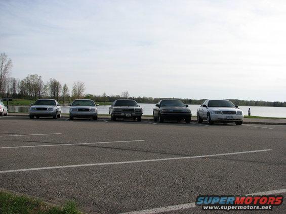 Four Ford Crown Victorias parked in a lot, three silver and one black, facing forward