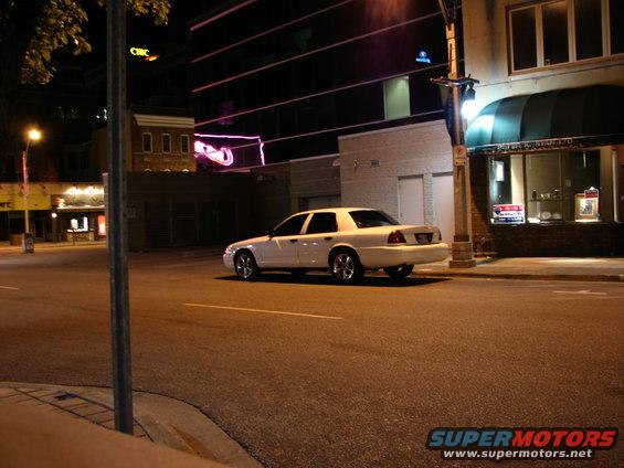White 2003 Ford Crown Victoria parked on a city street at night. The car is seen from the rear