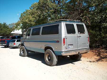 Silver 1978 Ford E250 van with blue trim and off-road tires, rear view