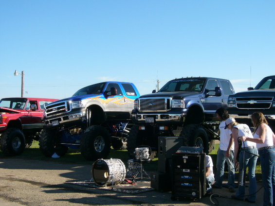 Blue and silver monster truck with custom graphics, parked next to a black pickup truck and a red SUV