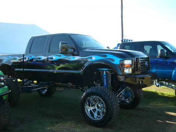 Lifted black Ford F-Series truck with blue flames and chrome wheels, parked next to a blue truck