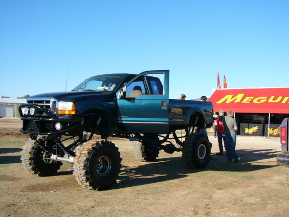 Lifted teal and black pickup truck with large tires and custom bumper