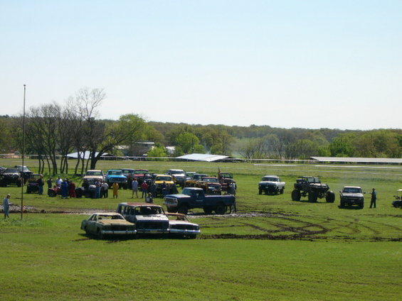Many trucks, SUVs, and cars gathered in a grassy field with some muddy patches
