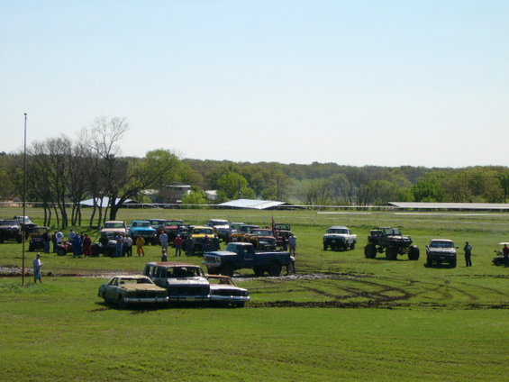Many trucks and cars gathered in a grassy field with some mud tracks visible