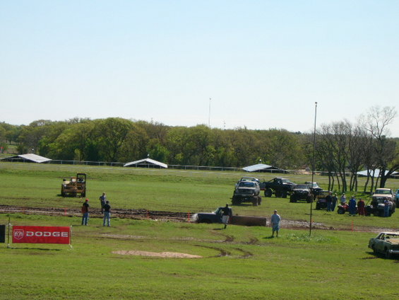 Mud pit scene with lifted trucks and people watching. Dodge banner visible