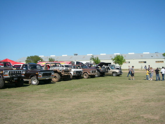 Line of 1978 Ford Broncos and other trucks parked on grass in front of a building