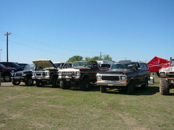 Several Ford Bronco SUVs parked on grass under a clear blue sky. One has its hood open