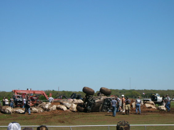 Off-road vehicle overturned on rocks with people gathered around