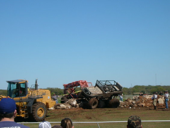 Yellow loader next to two off-road vehicles stuck in mud. One vehicle is red, the other is camouflaged
