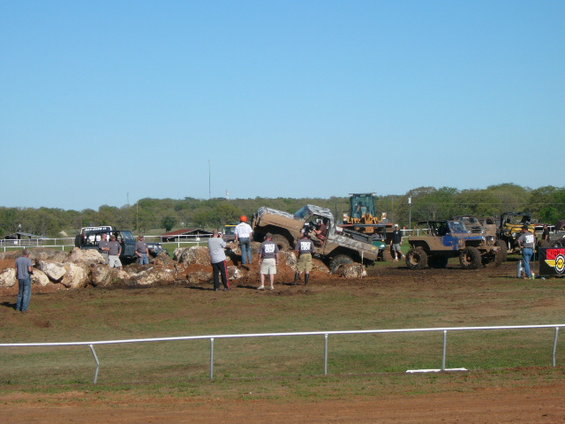 Muddy off-road vehicles navigating a rocky obstacle course with spectators