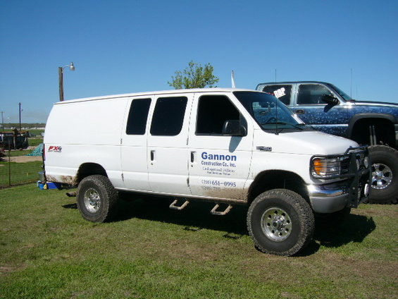 White Ford E-Series van with "Gannon Construction Co., Inc." text and phone number, parked on grass next to a blue pickup truck