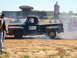 1978 Ford Bronco - A vintage pickup truck performs a burnout at an outdoor event, with large inflatable advertising signs visible in the background.