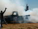 1978 Ford Bronco - A black pickup truck performs a burnout, surrounded by smoke, with a giant Dr. Pepper bottle in the background.