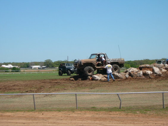 Muddy off-road truck with big tires navigating rocks, another SUV nearby