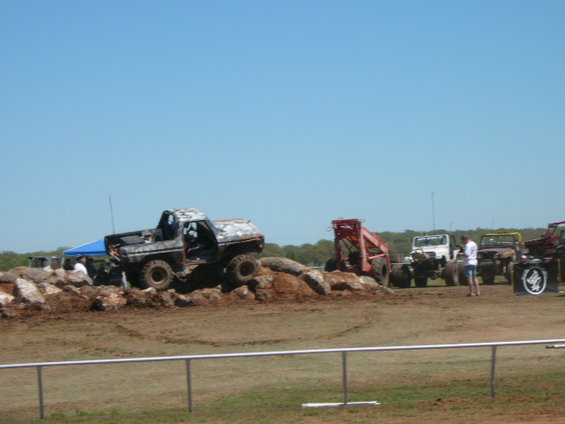 muddy off-road vehicles on rocky terrain, some jeeps and a truck in background