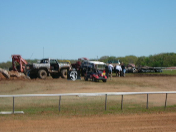Several off-road vehicles, including a lifted truck and a golf cart, gathered in a grassy field with people standing around