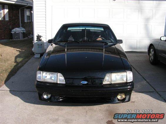 Black 1988 Ford Mustang parked in front of a garage. Another car is visible to the right