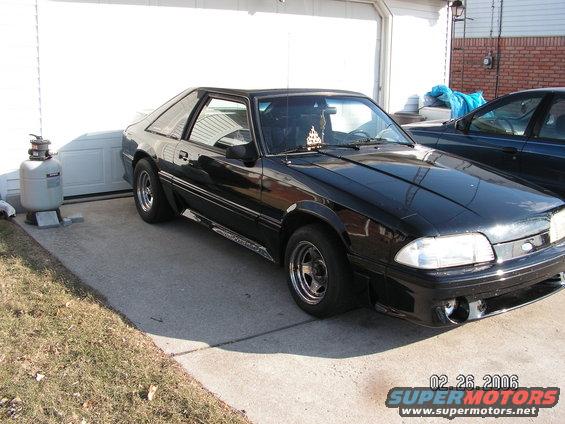 Black coupe parked in front of a garage, another car is parked to the right