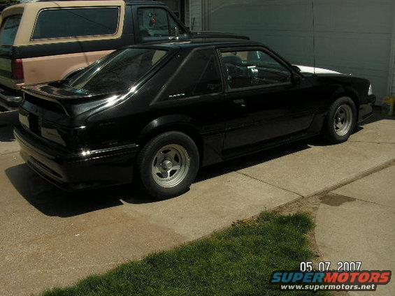 Black coupe with a rear spoiler, parked on a driveway next to a tan SUV