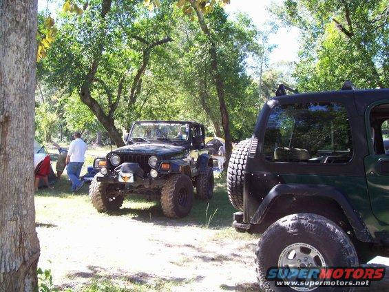 Two Jeeps parked in a wooded area with tents and people