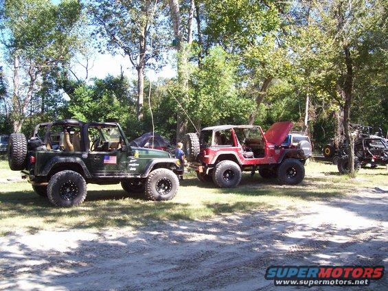 Two Jeeps, one green and one red, parked on a dirt path with trees in the background