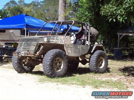 Mud-covered off-road buggy with roll cage, large tires, and spare tire on the back