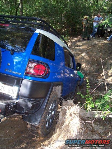 Blue Toyota FJ Cruiser stuck in mud on a wooded trail with people watching