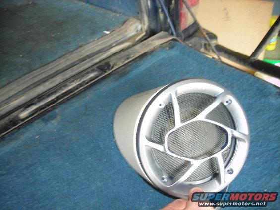 Car speaker with silver grille, resting on blue carpeted surface