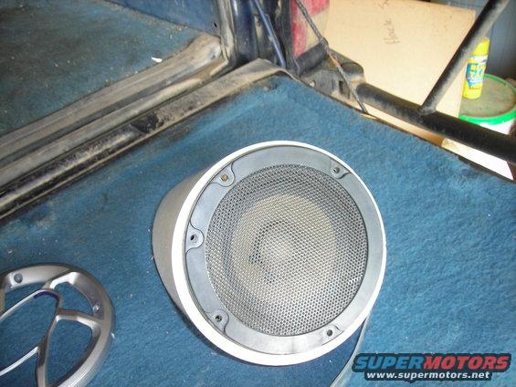 Car speaker with silver grille on blue carpet inside a vehicle