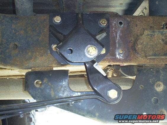 Close-up of a black metal suspension component bolted to rusty frame rails