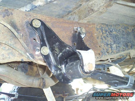 Black suspension part bolted to rusty frame, with visible Supermotors.net logo
