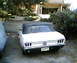 1968 Ford Mustang - Rear view of a white convertible parked in a driveway with trees and a building in the background.